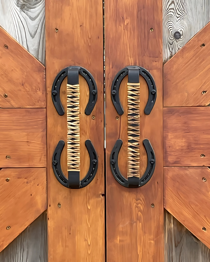 Horse shoe handles wrapped with leather braided handles mounted on barn doors outside.