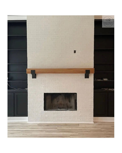 Heavy duty black steel mantel brackets supporting natural wood beam on white brick fireplace surround with dark built-in s...