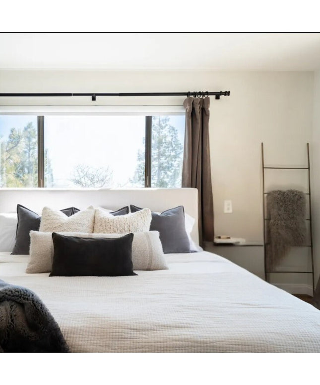 Black metal decorative ladder from Industrial Farm Co leaning against bedroom wall, displaying gray throw blanket in moder...