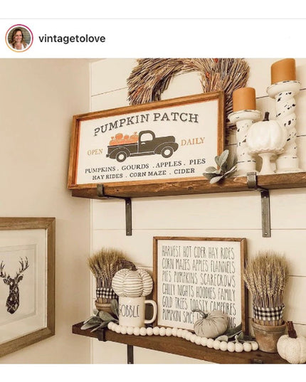 Black metal shelf brackets supporting rustic wood shelves with fall decor including pumpkin patch sign, wheat bundles, and...