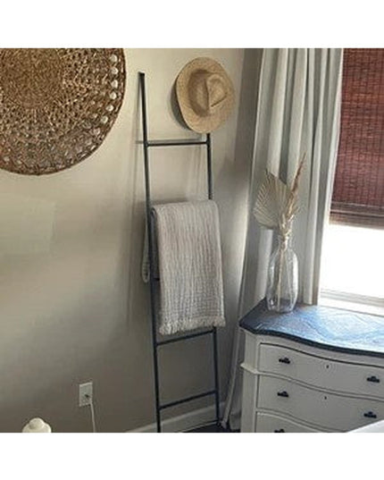 Black metal ladder shelf displaying white textured throw blanket in modern farmhouse bedroom corner with woven wall decor ...