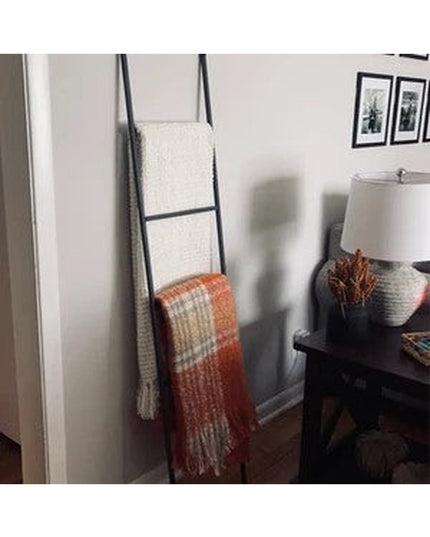 Black metal decorative ladder with white and orange plaid throw blankets displayed in modern living room corner by Industr...