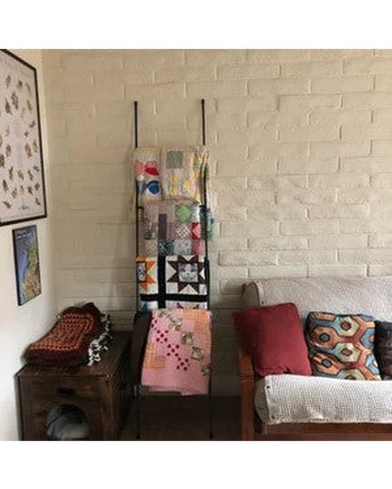 Black metal Lynn ladder from Industrial Farm Co displaying colorful quilts and blankets in cozy living room with white bri...