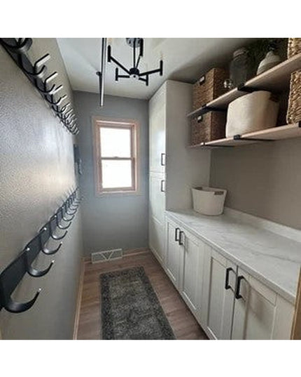 Narrow laundry room with black metal J-hook shelf brackets mounted on wall holding wicker baskets, white cabinets below, m...