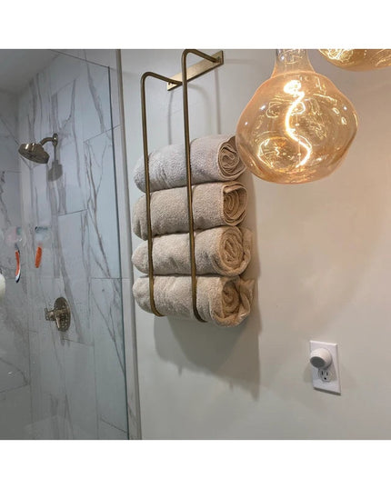 Industrial Farm Co Tyler brass metal towel rack mounted on bathroom wall holding rolled beige towels next to marble shower