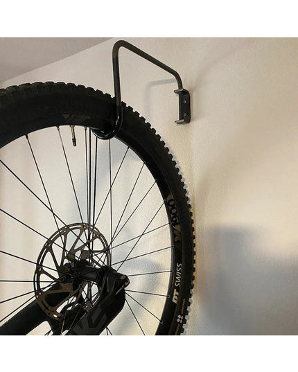 Black wall-mounted bike rack holding mountain bike wheel with disc brake against white wall - The Logan Hook by Industrial...