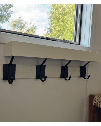 Four black metal Felix Wall Hooks mounted on white wainscoting below a window, showing modern farmhouse style coat hooks b...