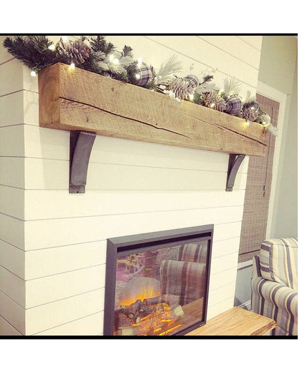 Rustic wooden Jeffery Style Shelf Brackets supporting reclaimed wood mantel with Christmas garland above white shiplap fir...